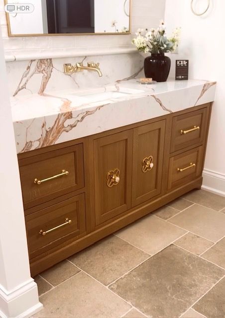 Luxury bathroom vanity with white marble countertop, gold faucet, and wood cabinets on a tiled floor