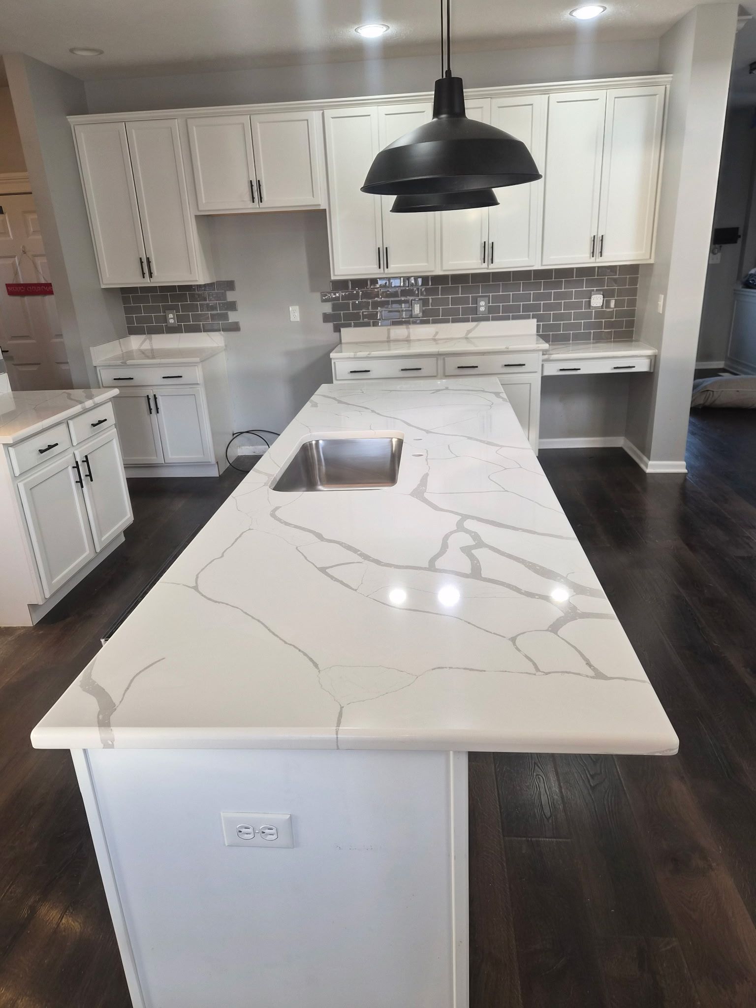 Modern white kitchen with large marble island, black pendant lights, and dark wood flooring