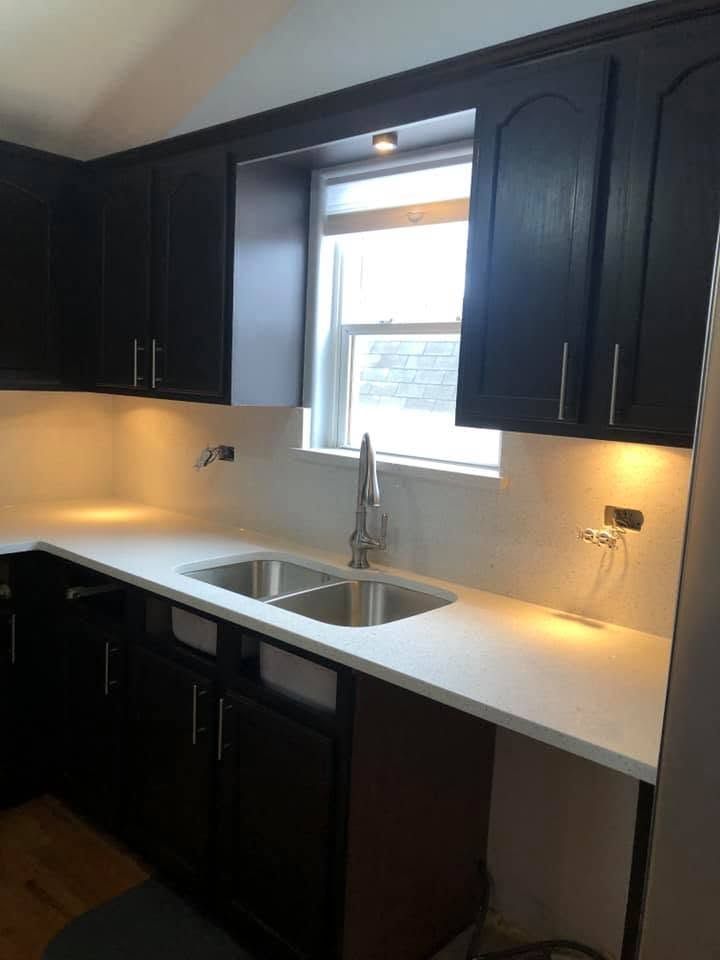 Dark kitchen with black cabinets, white countertops, and a window over the sink.