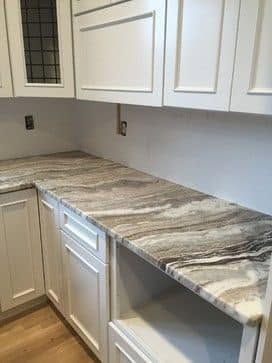 White kitchen countertops with gray-veined marble-look surface, white cabinets, and wood floor
