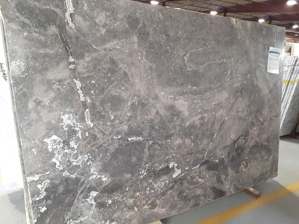 Large gray marble slab standing upright in a warehouse aisle, with white veining and chips.