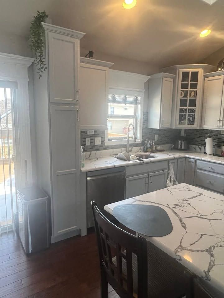 Bright kitchen with white cabinets, marble island, stainless dishwasher, and dark wood floor.