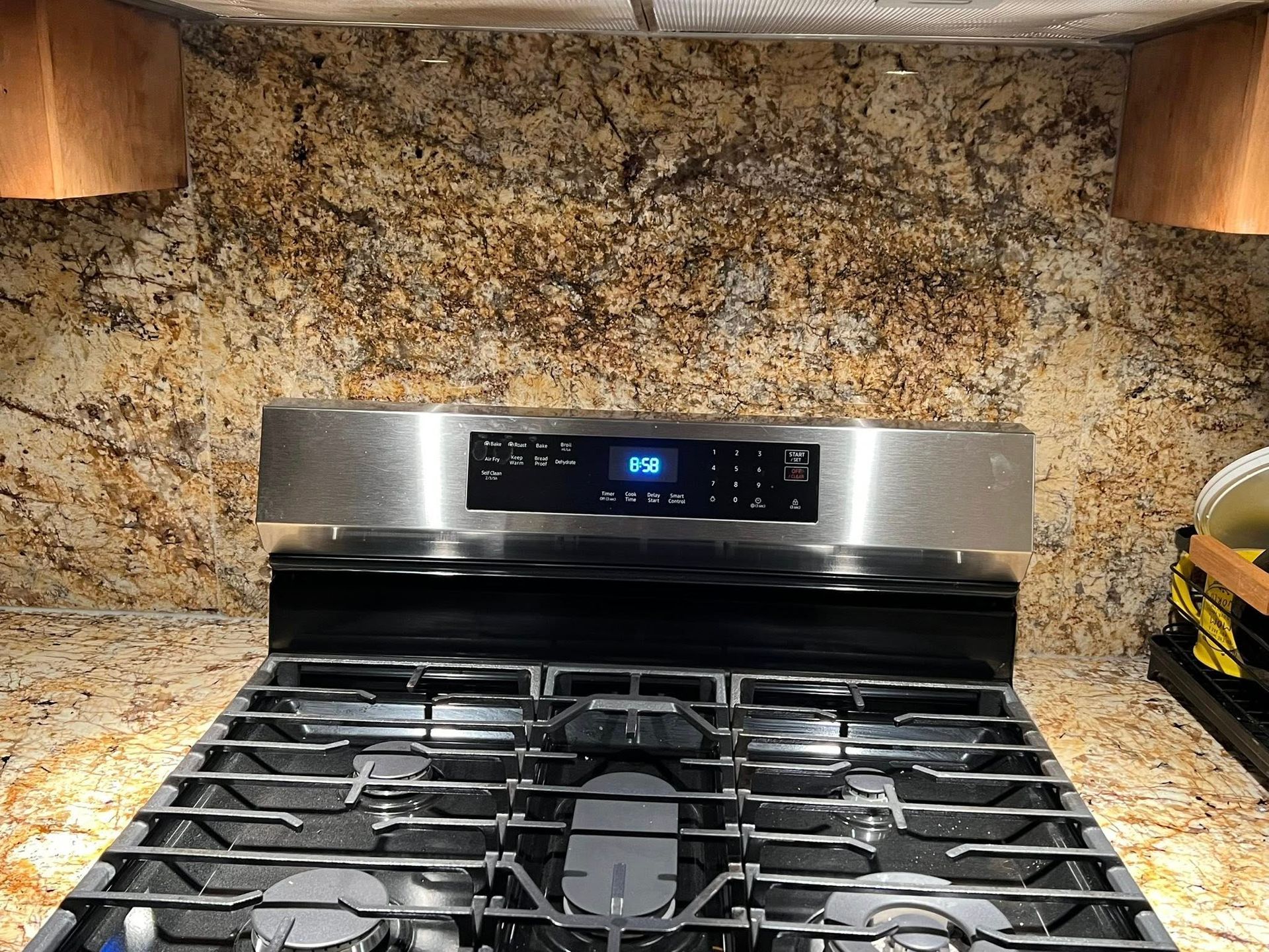 Stainless steel gas range with black grates against a speckled granite backsplash.