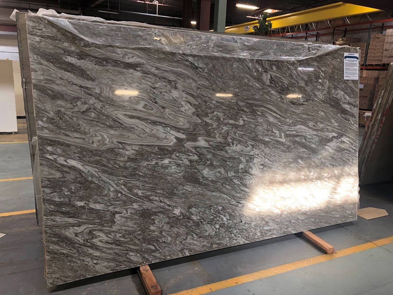 Large polished gray stone slab with white veining in a warehouse or stone yard.