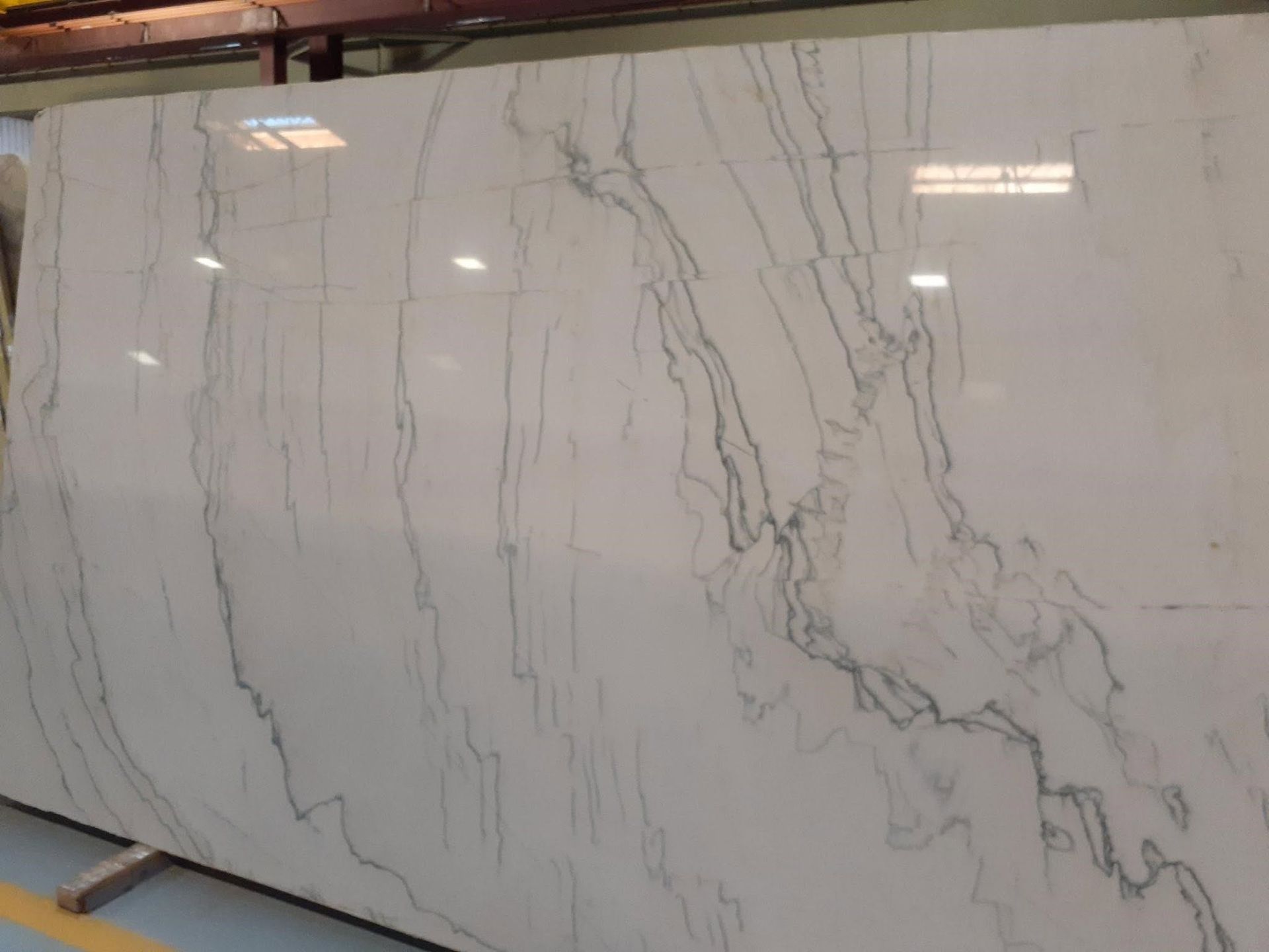 Large white marble slab with gray veining displayed upright in a warehouse or showroom.