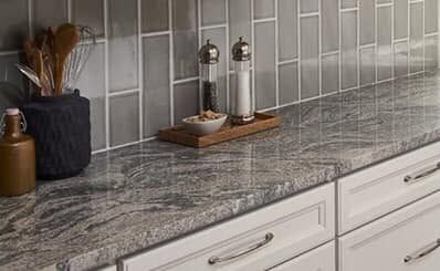 Kitchen countertop with gray tile backsplash, granite surface, and decorative canisters and utensils.