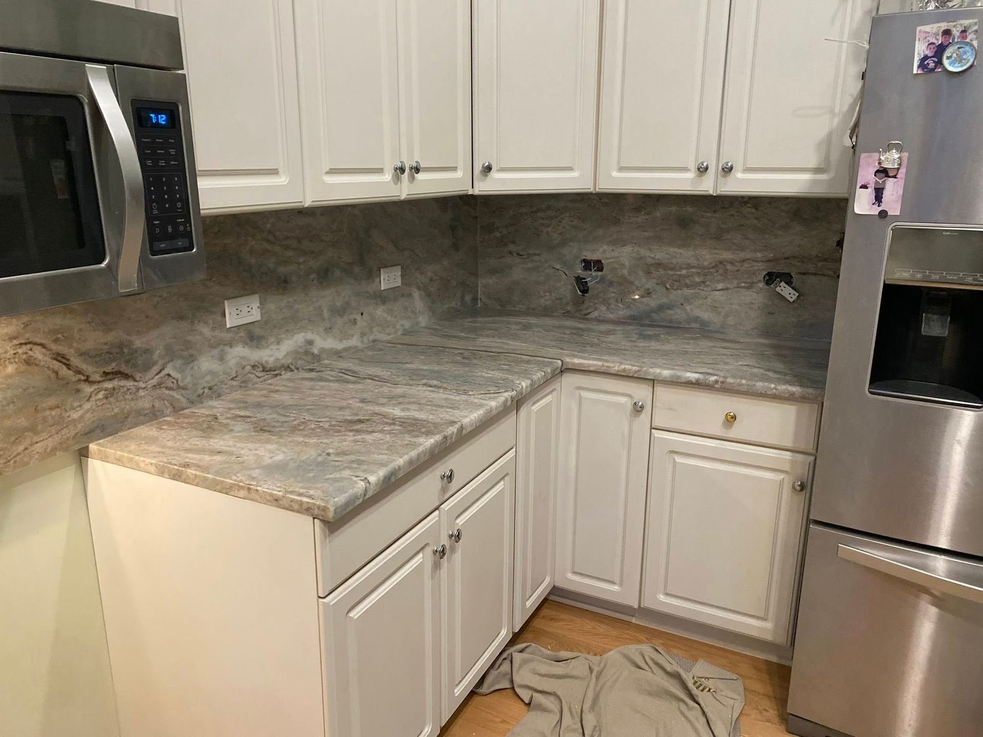 Bright kitchen corner with white cabinets, granite countertops, and stainless steel appliances