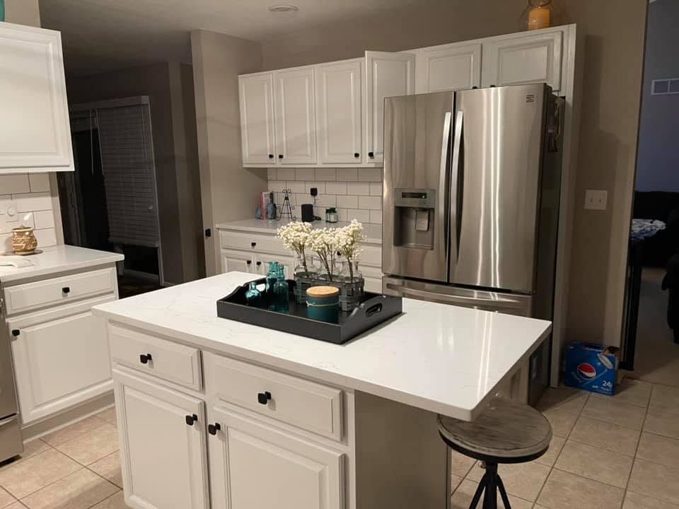 Bright modern kitchen with white cabinets, stainless steel fridge, and a central island with decor.