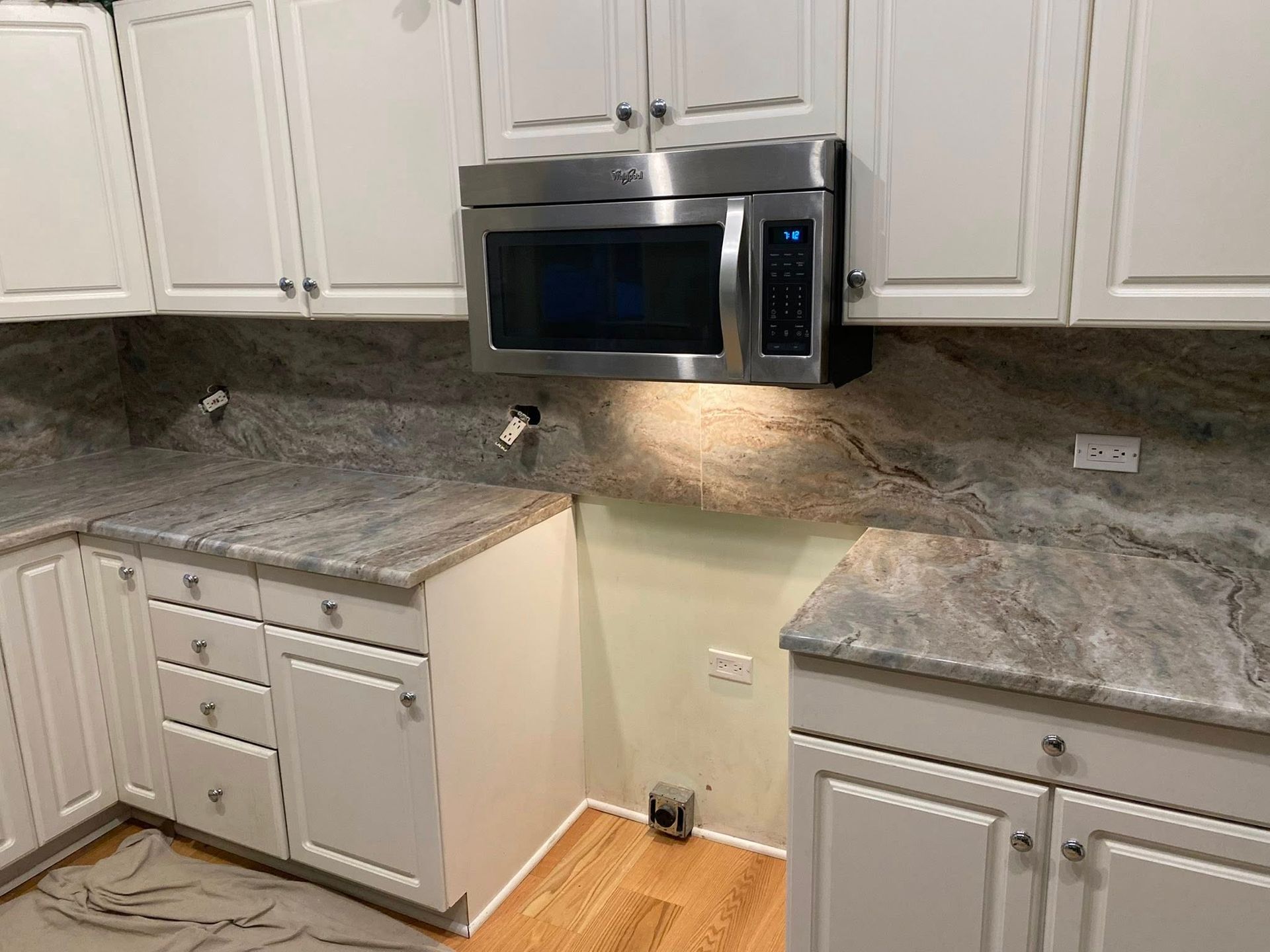 Kitchen corner with white cabinets, gray countertops, and a stainless steel microwave above the counter