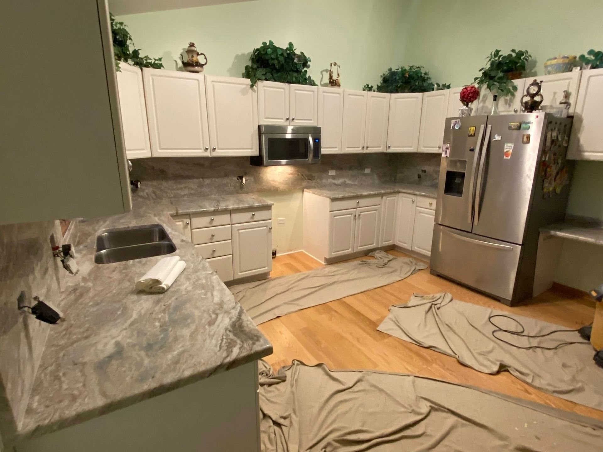 Modern kitchen with white cabinets, stainless steel appliances, marble island, and floors covered with drop cloths during renovation