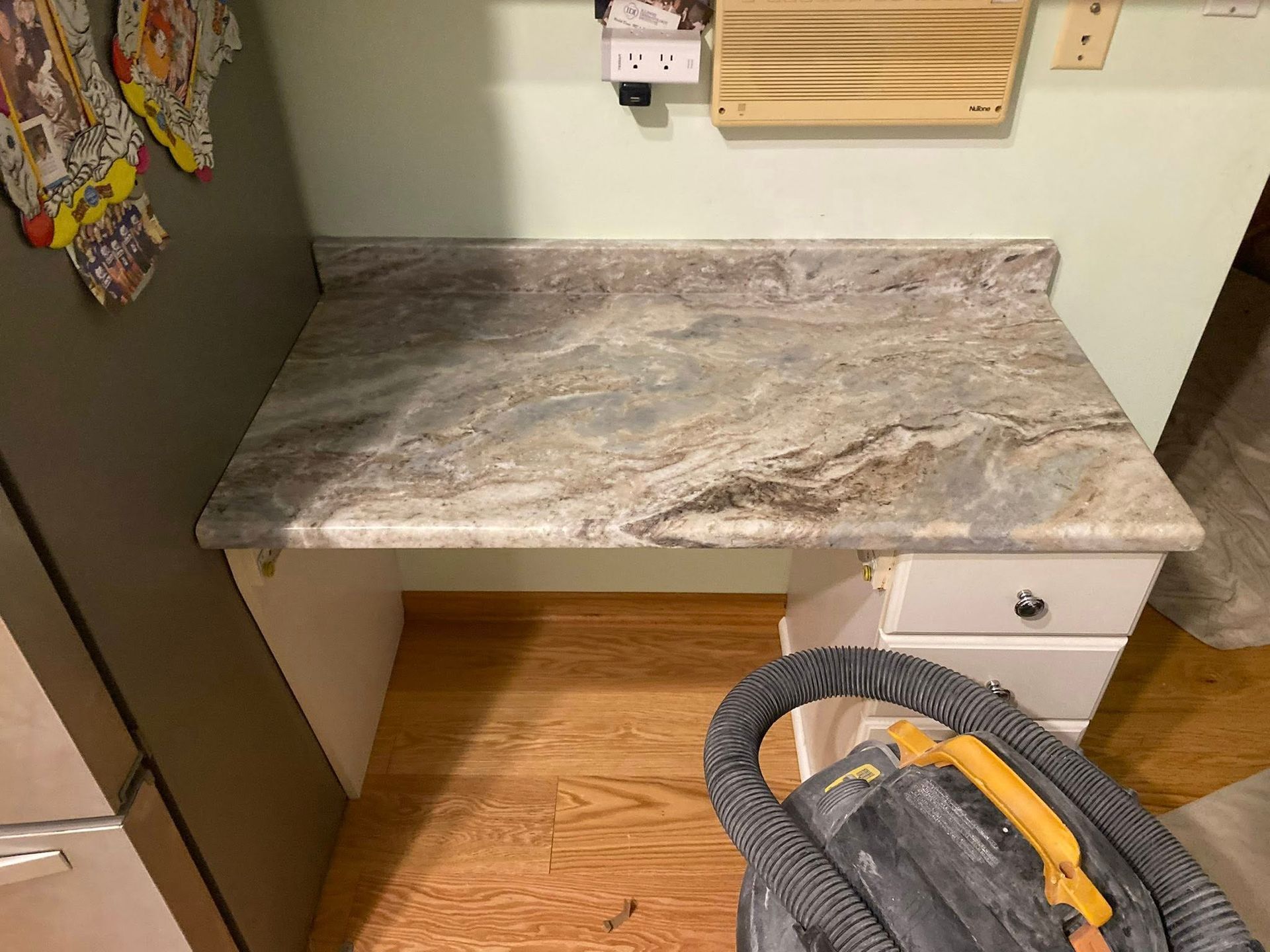 Gray marble-look countertop in a kitchen workspace beside a refrigerator and vacuum cleaner.