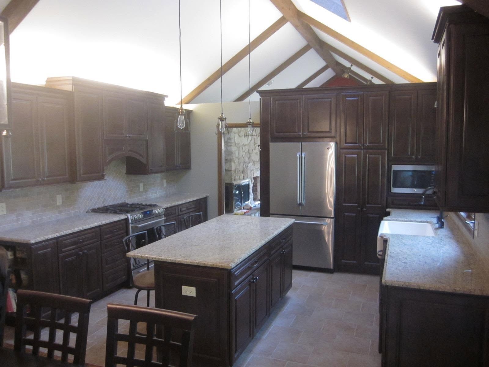 Modern kitchen with dark wood cabinets, stainless steel refrigerator, and central island under vaulted ceiling