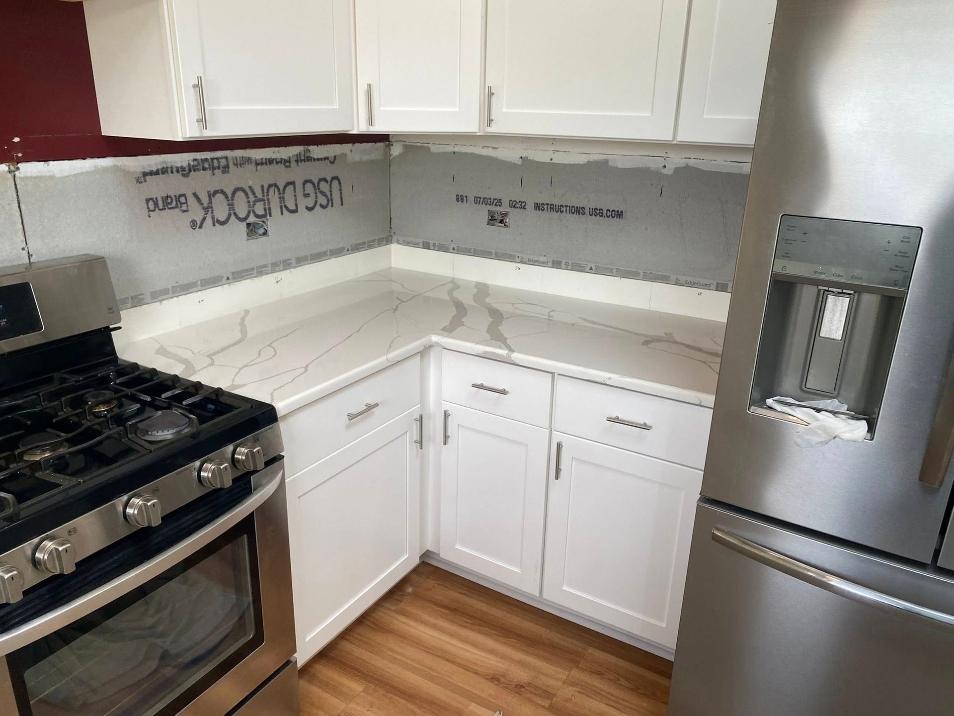 Small white kitchen corner with gas stove, sink counter, and stainless steel refrigerator.