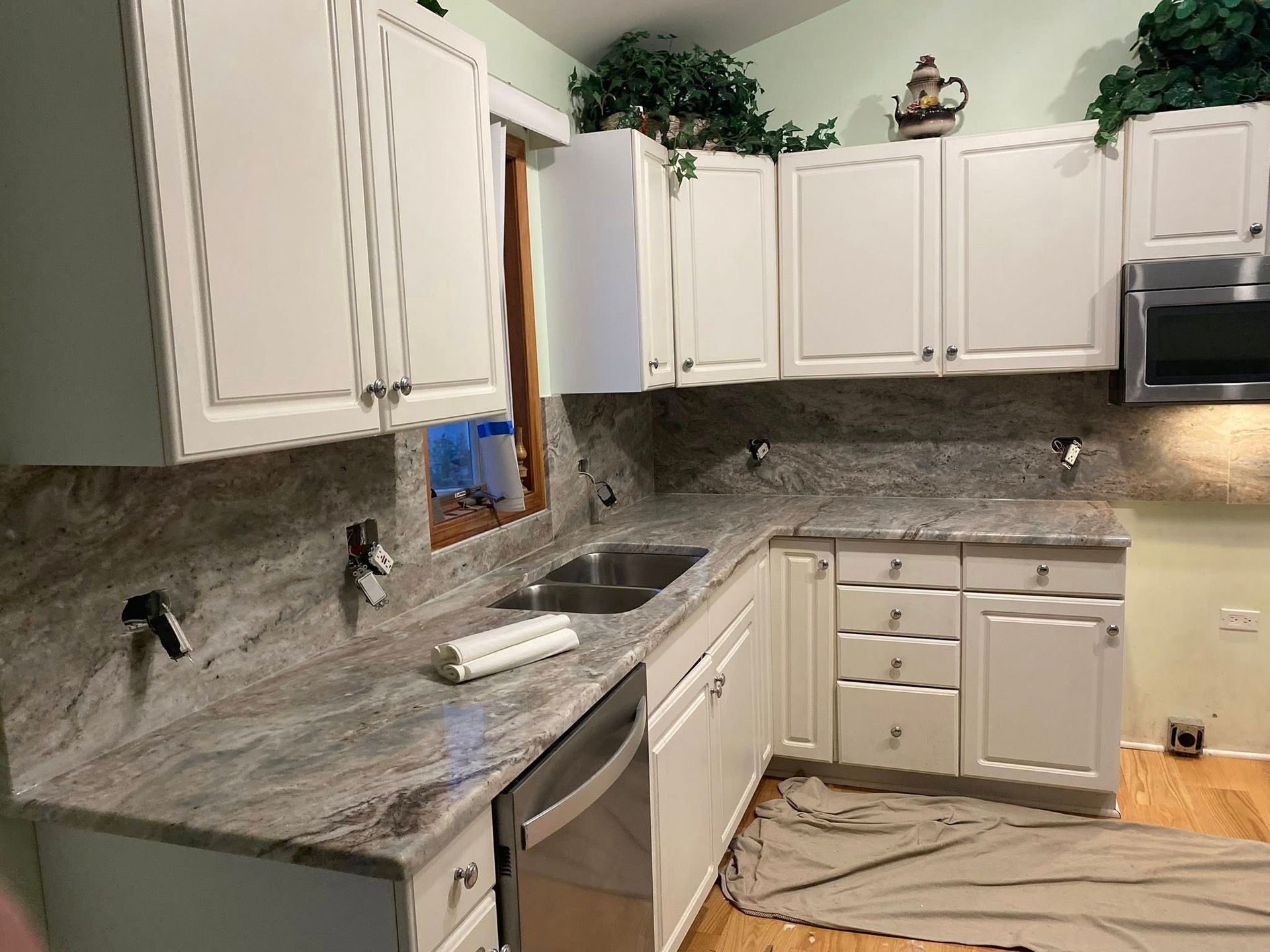 Bright white kitchen with granite countertops, white cabinets, stainless dishwasher, and a small window.