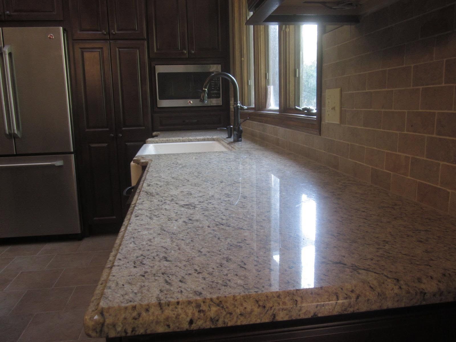 Granite kitchen island countertop with sink, stainless fridge, and dark wood cabinets