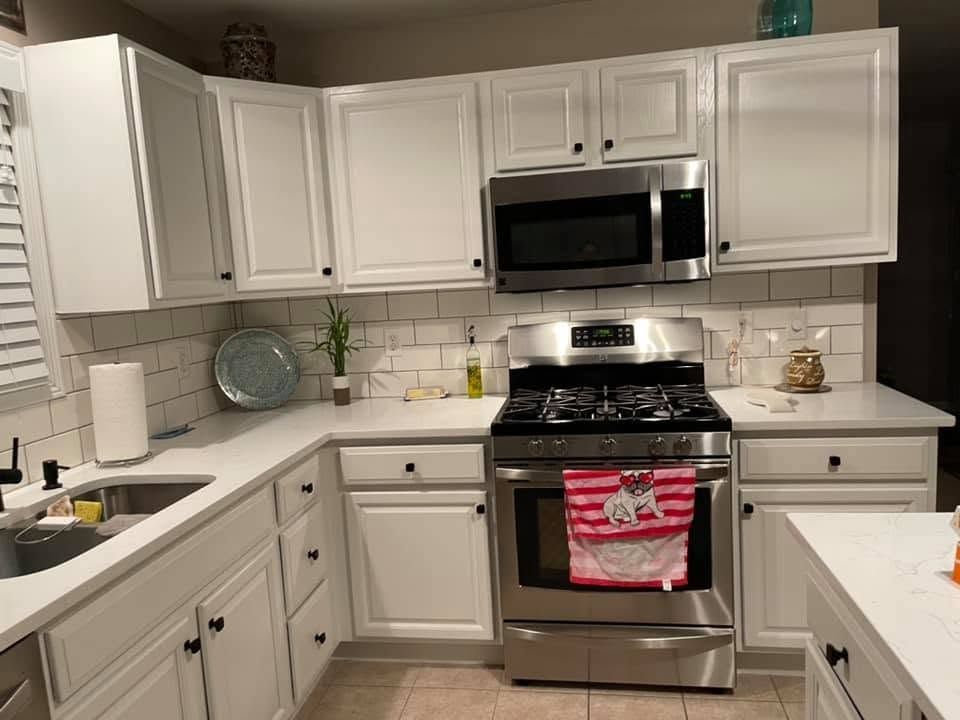 Bright white kitchen with stainless steel stove and microwave, white cabinets, and counter decor.