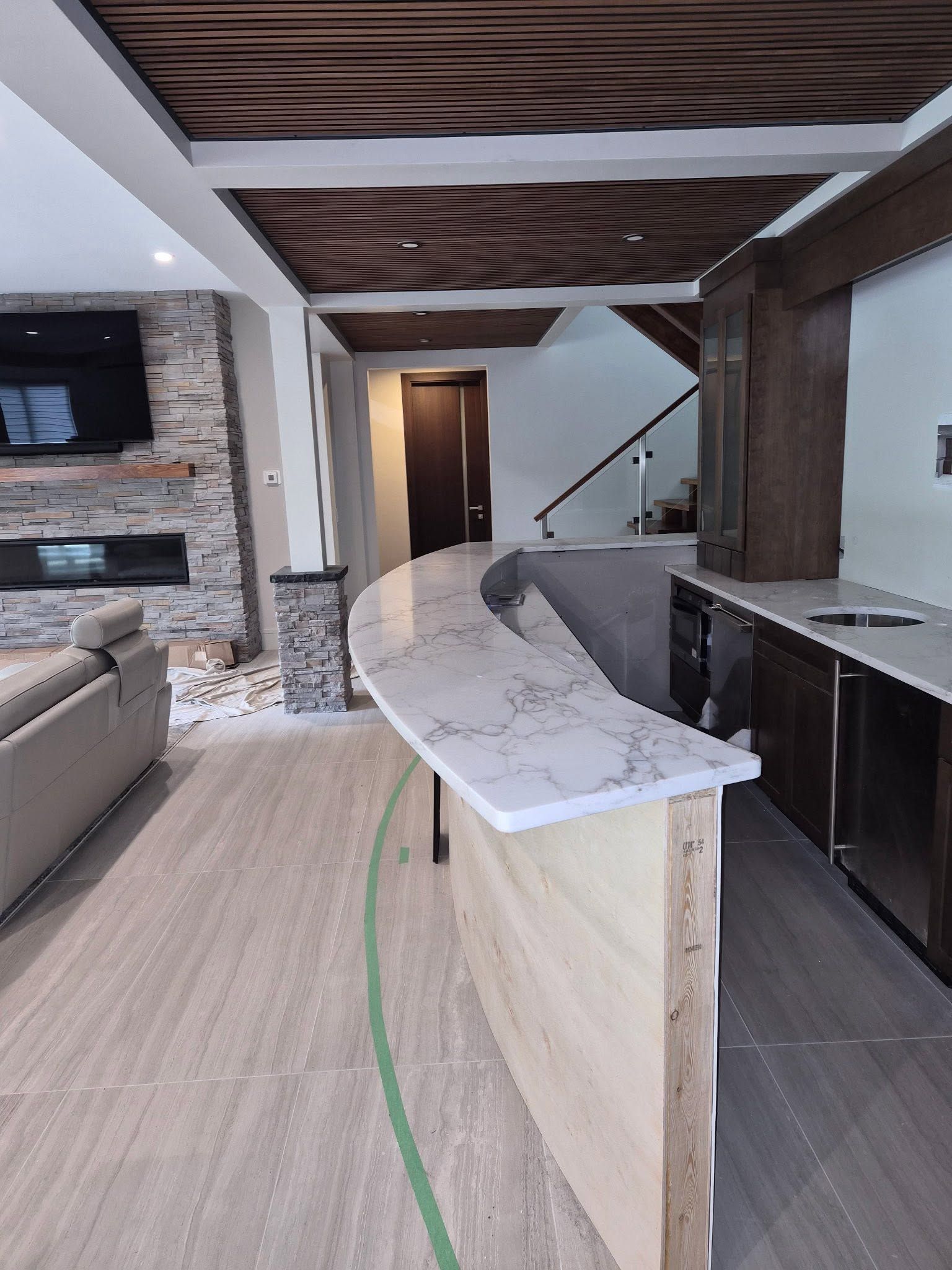 Modern kitchen with curved island, wood ceiling beams, stone accent wall, and bar seating