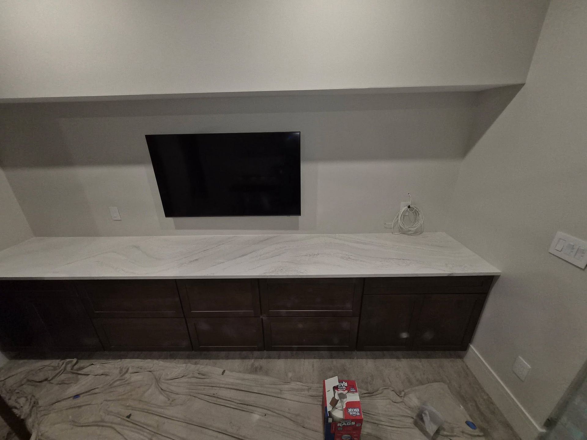Empty room with dark wood cabinets, white marble countertop, and a black wall opening under a shelf.