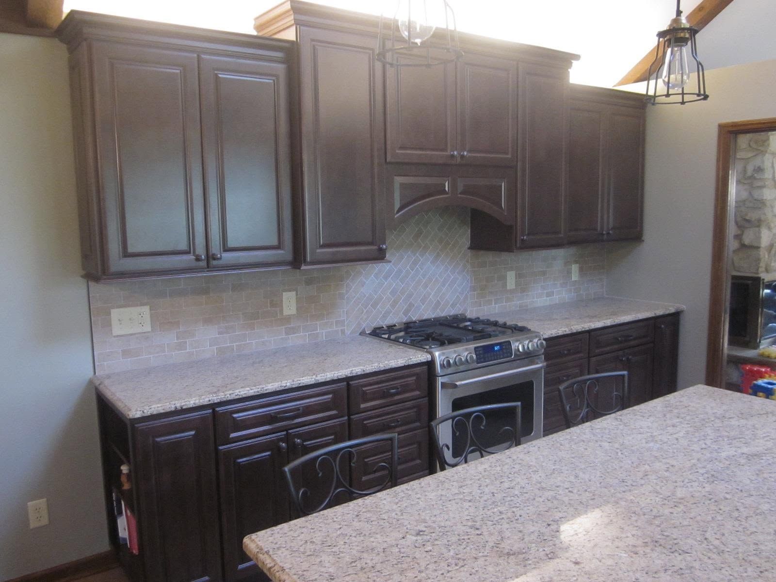 Dark wood kitchen cabinets with granite countertops, stove, and island in a bright kitchen