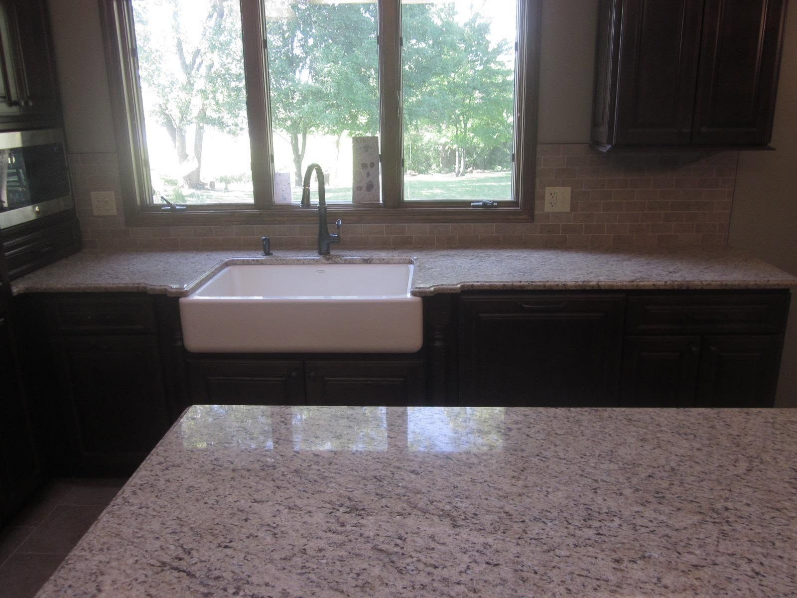 Kitchen with white apron sink beneath a window, granite countertops, and dark cabinets