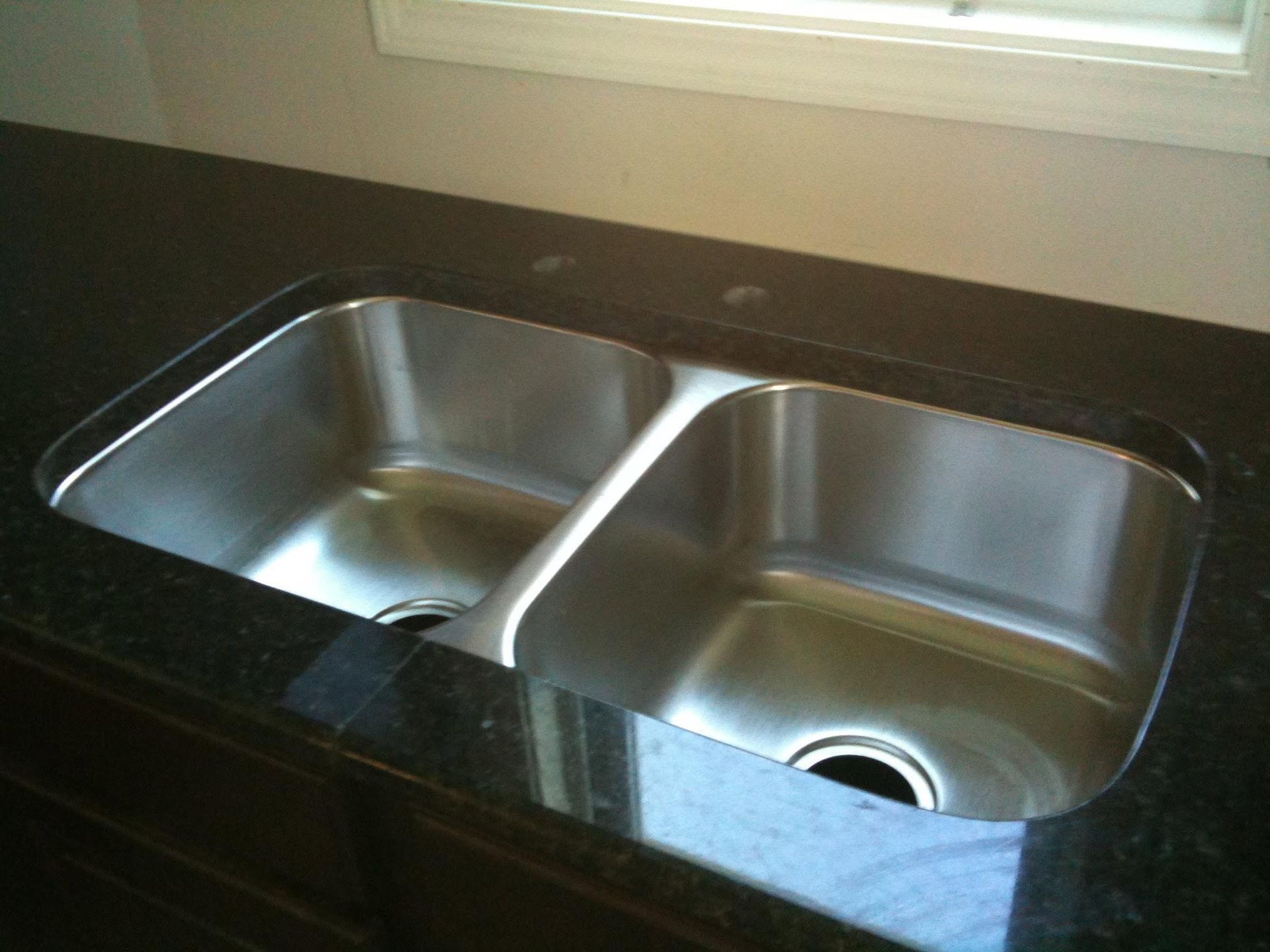 Double-basin stainless steel kitchen sink with black countertop and window above