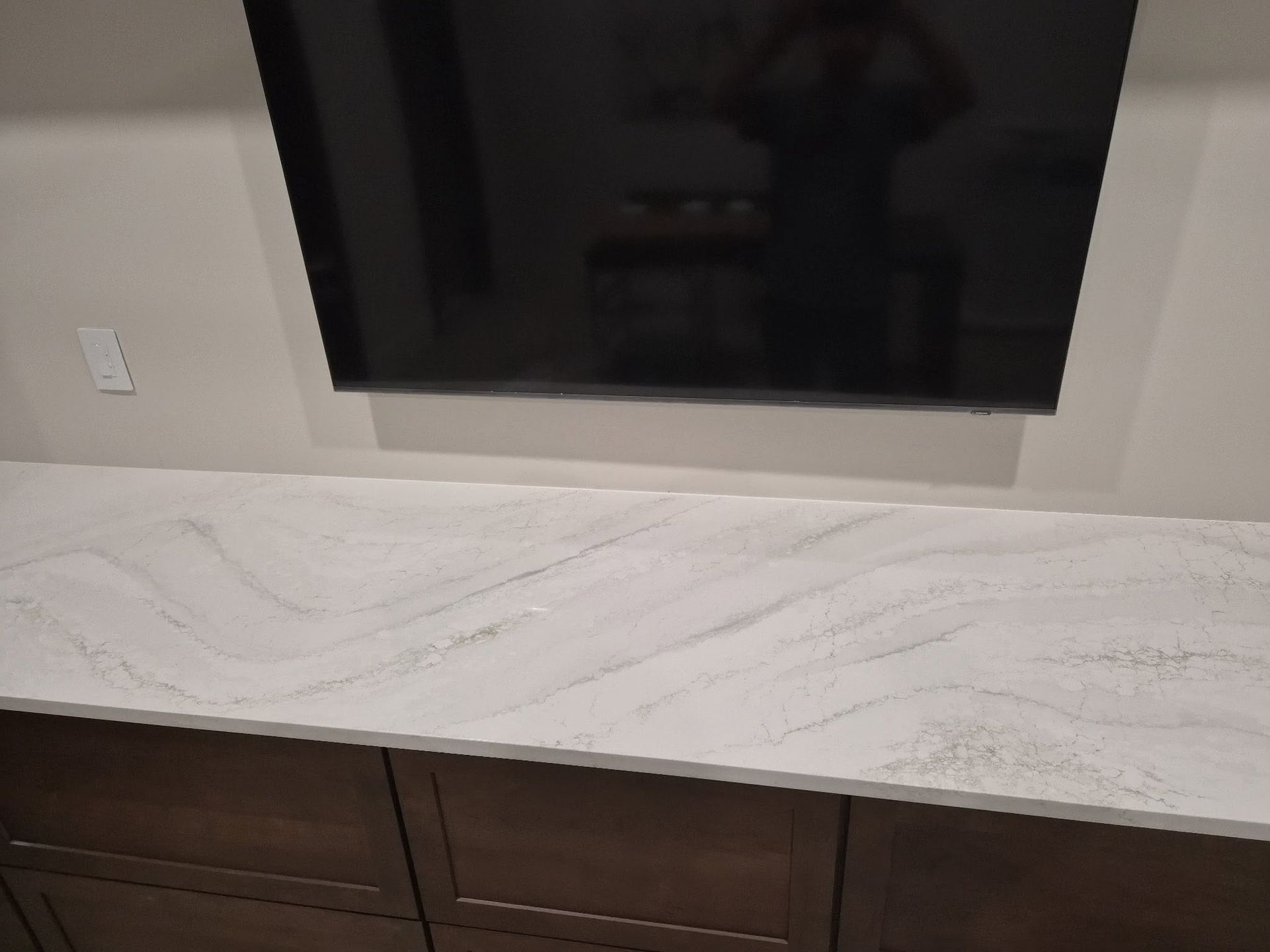 Wall-mounted TV above a light stone countertop and dark wood cabinets in a modern room