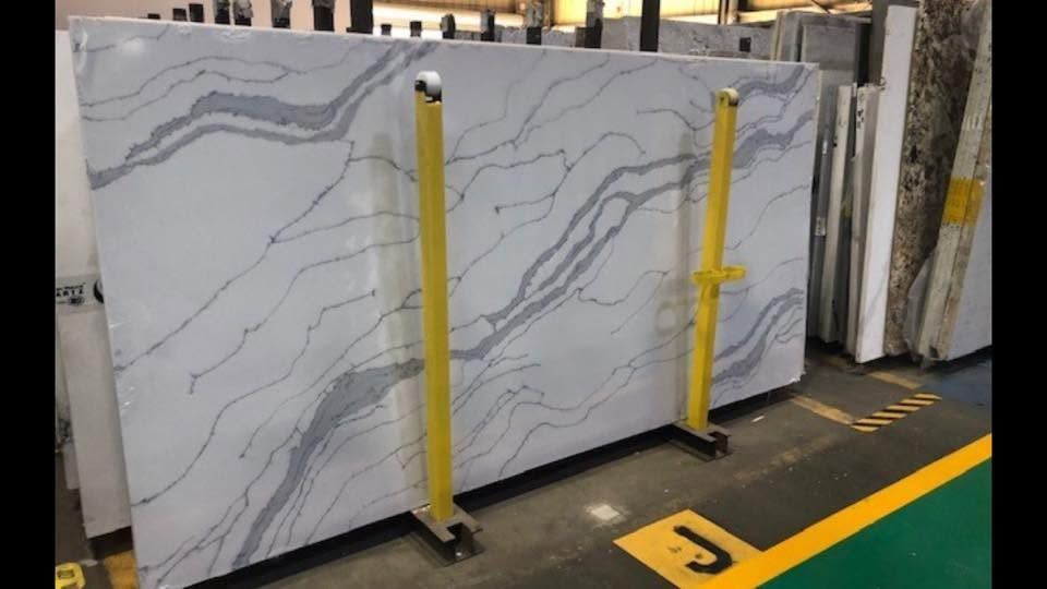 Large white marble slab with gray veining standing upright on yellow supports in a warehouse.