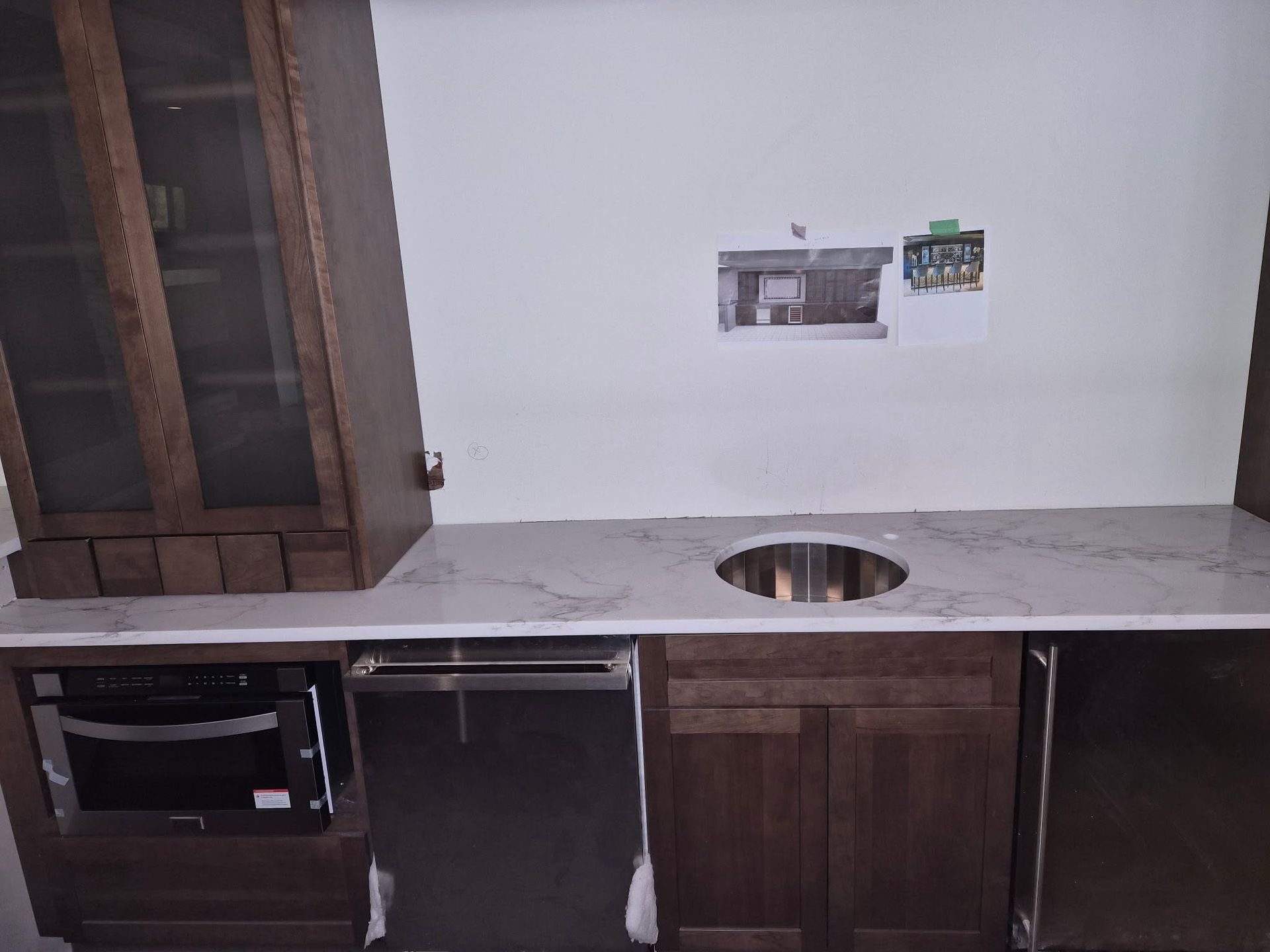 Unfinished kitchen with dark wood cabinets, marble countertop, sink cutout, and built-in oven space.