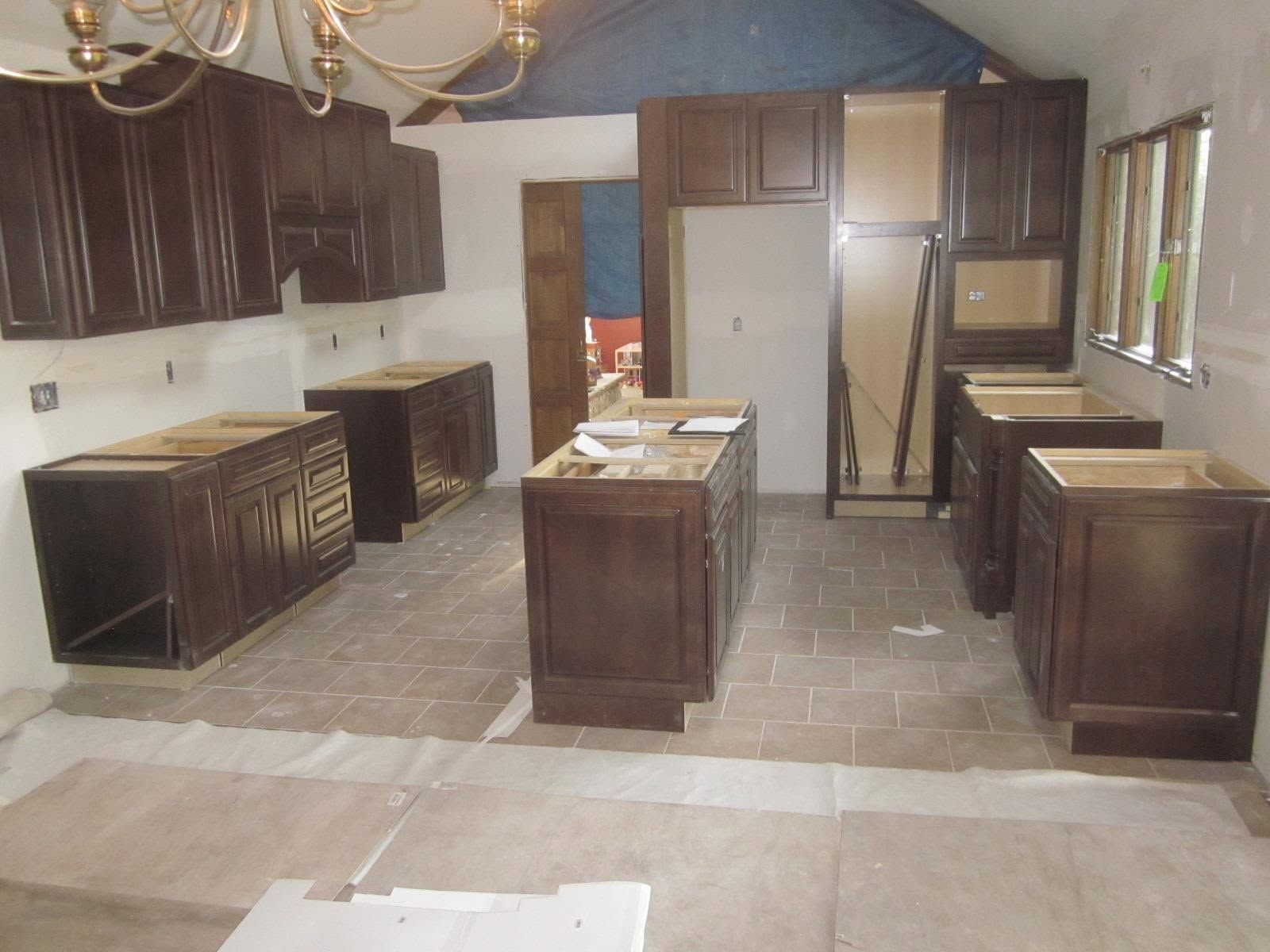 Empty kitchen with dark wood cabinets and an island, under construction with tools and bare flooring