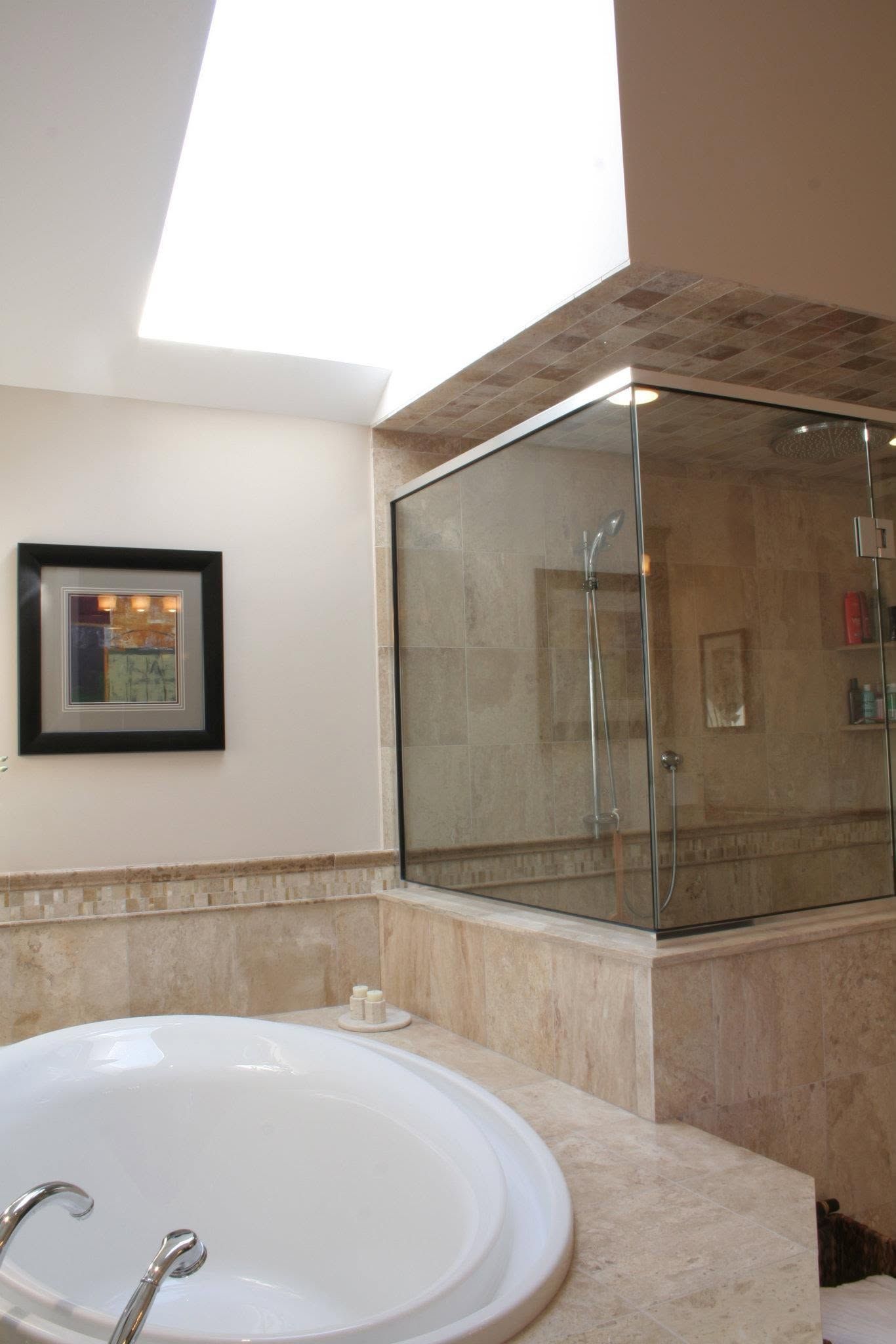 Bathroom with a white sink, beige tile counter, and glass-enclosed shower under a skylight