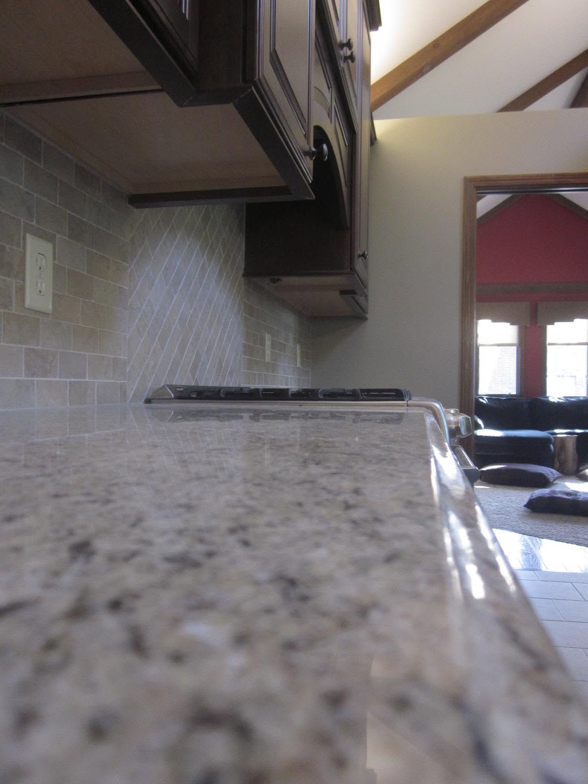 Granite countertop in a kitchen, with cabinets above and a tiled backsplash leading to a dining area.