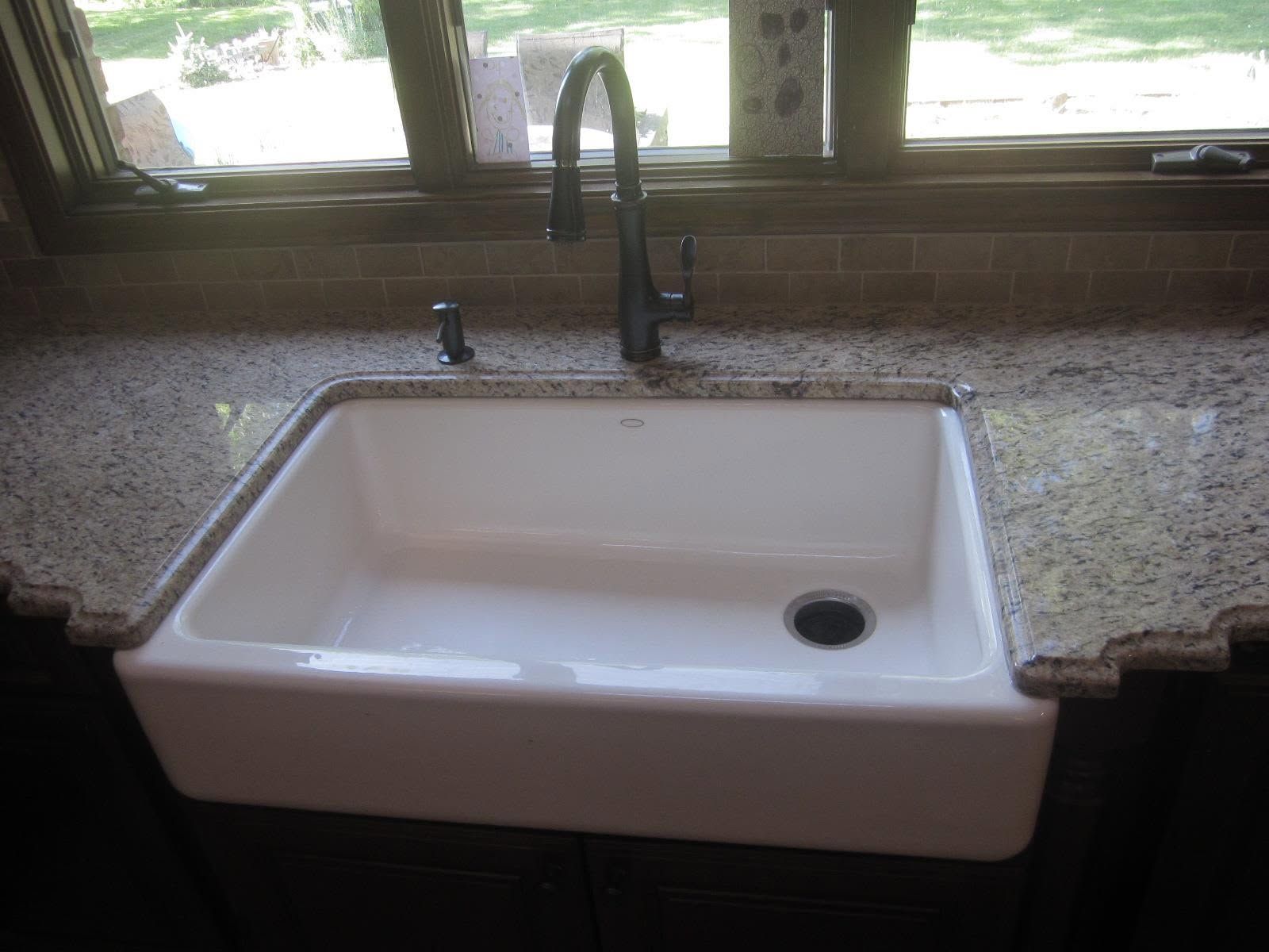 White kitchen sink with dark faucet set in a speckled granite countertop by a window.