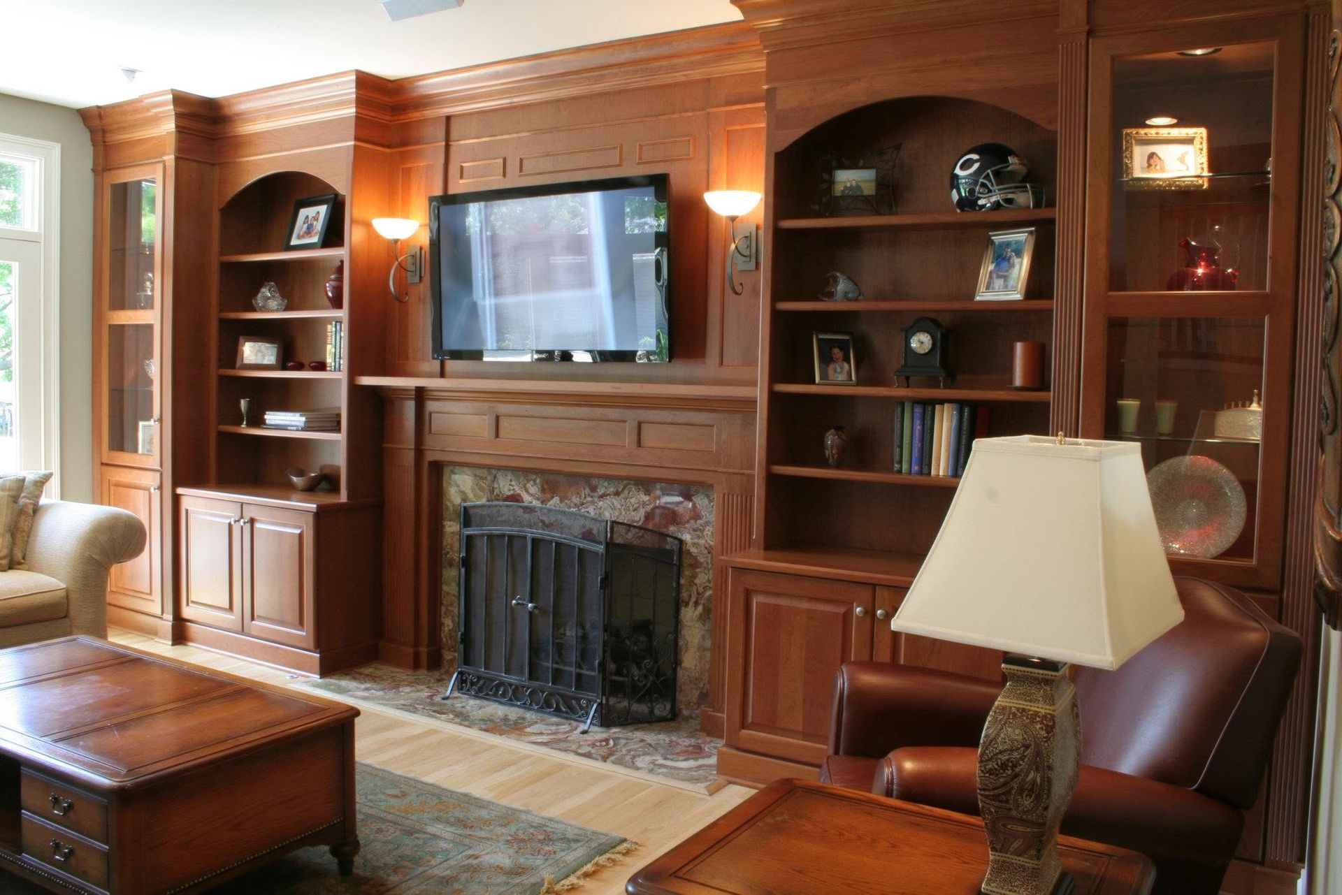 Wood-paneled living room with built-in shelves, TV above fireplace, and lamp beside a leather chair
