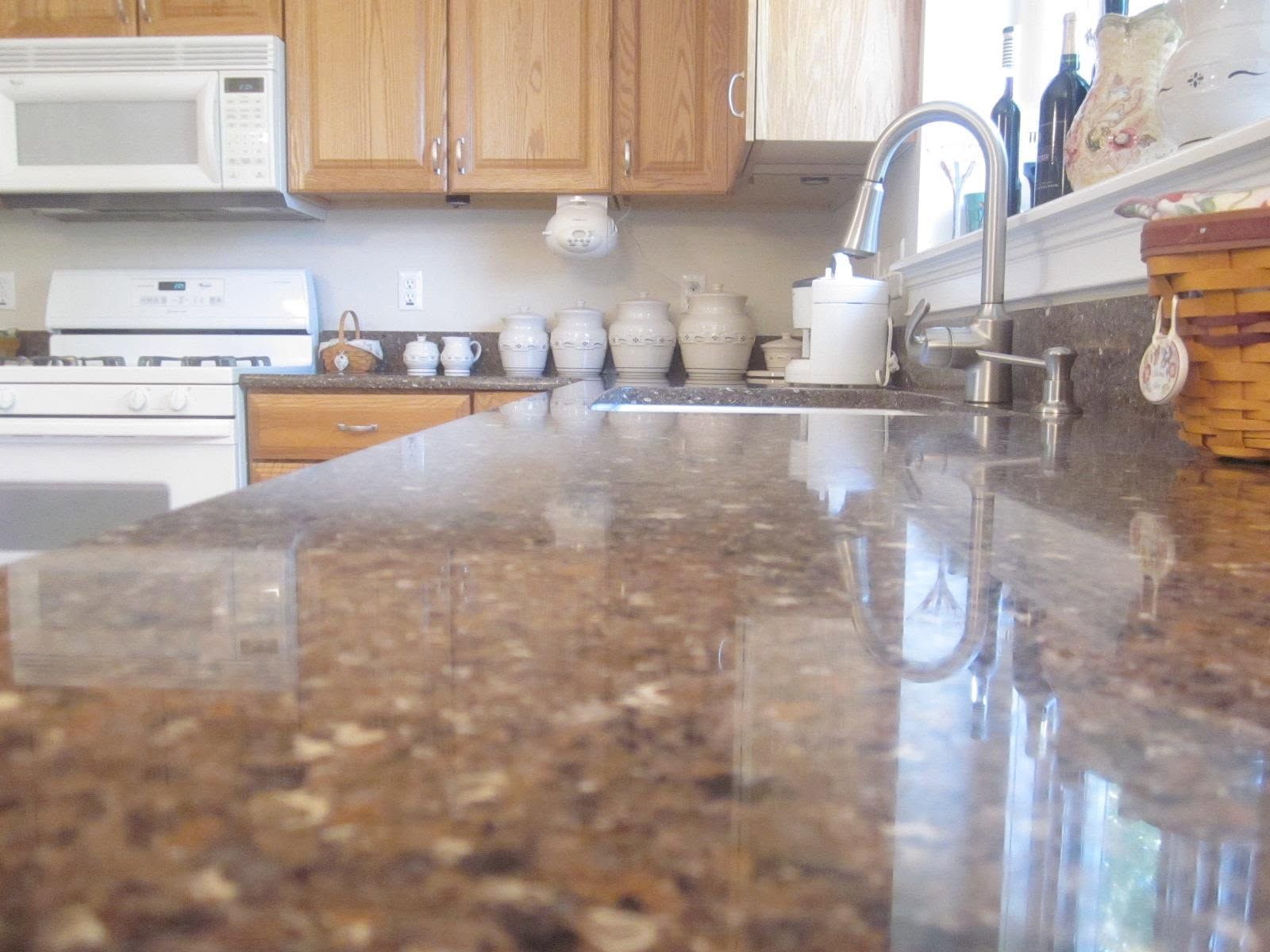 Kitchen countertop with granite surface, sink, wooden cabinets, and white appliances in the background