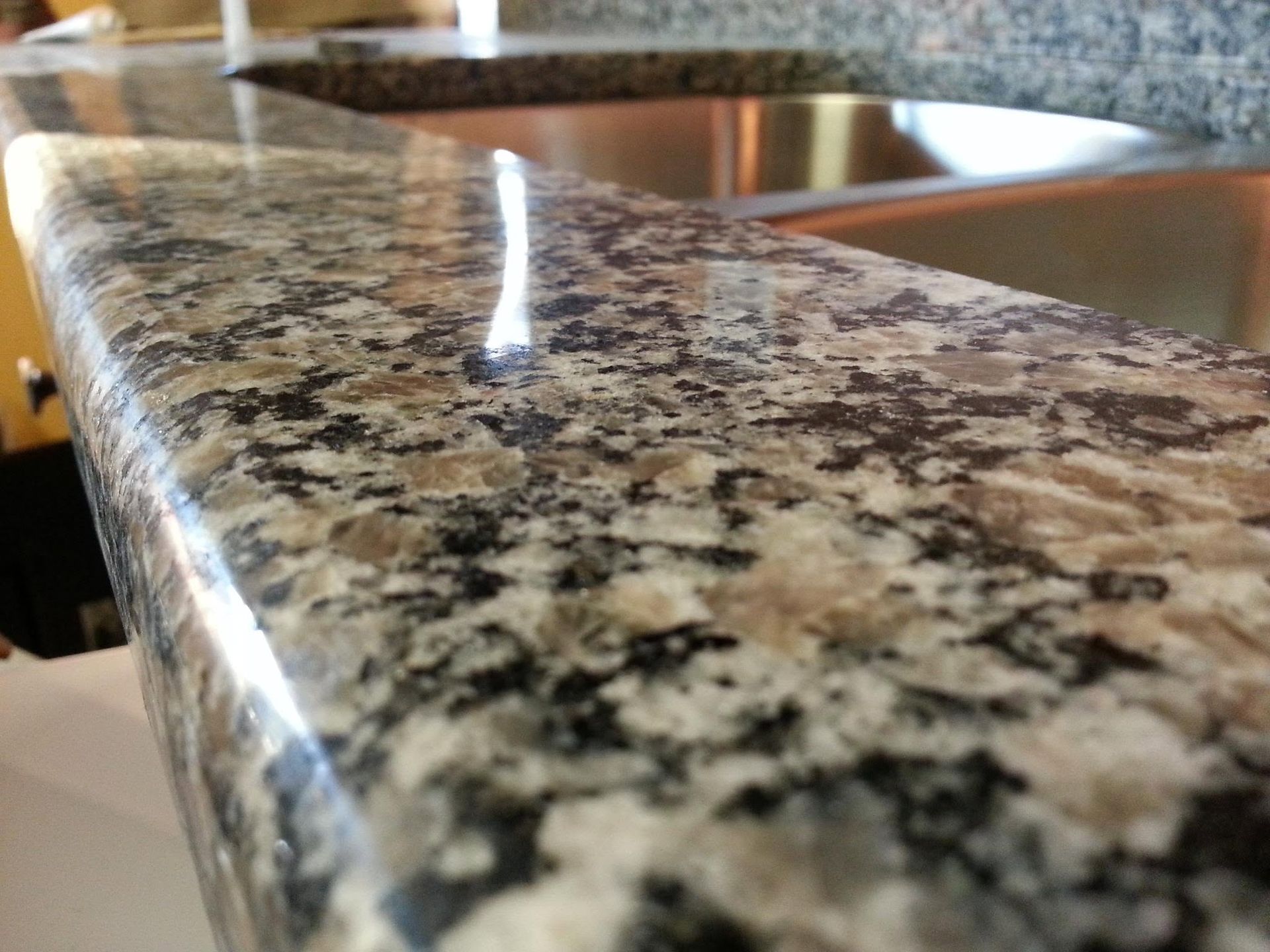 Close-up of a polished speckled granite countertop with a glossy reflection in a kitchen