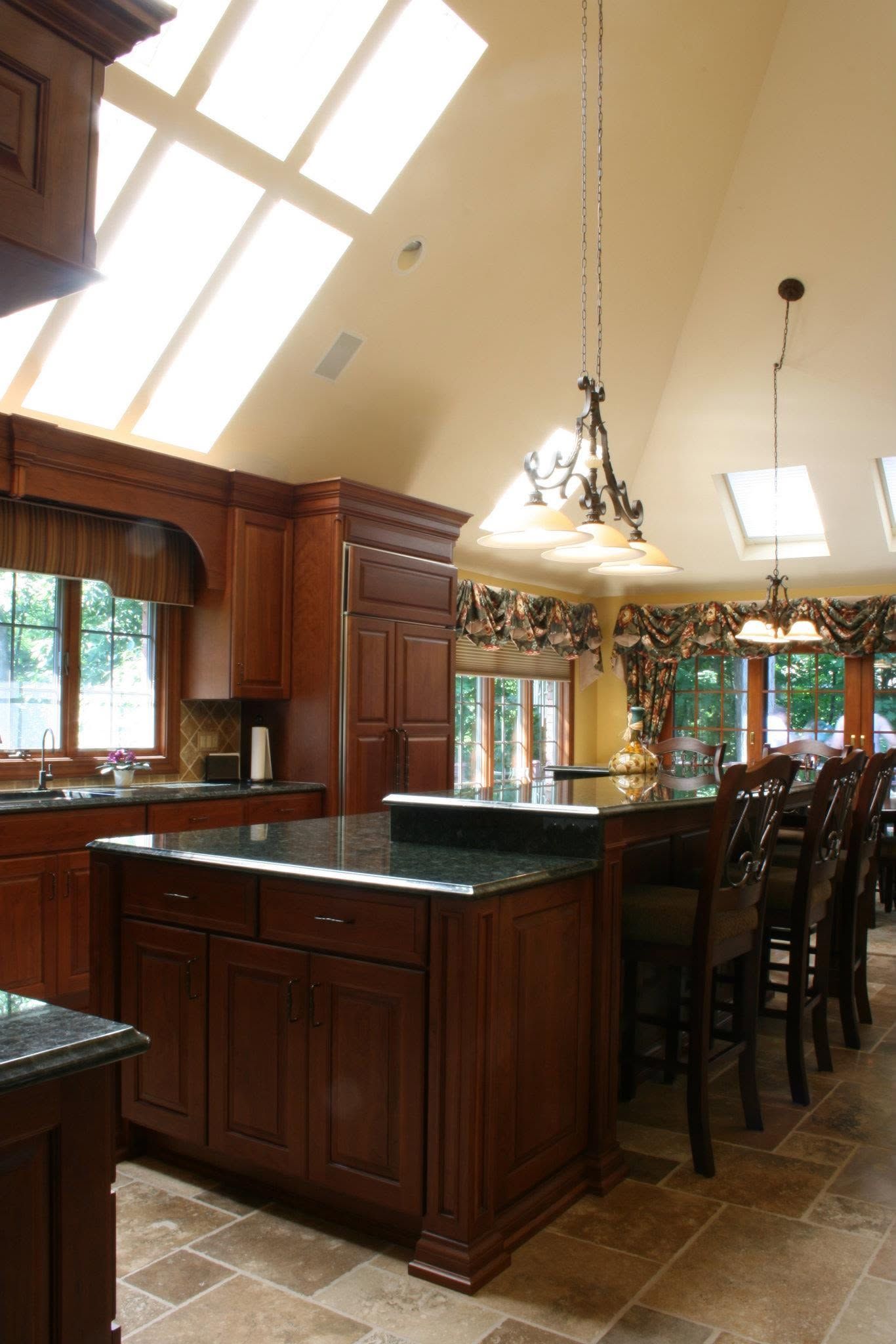 Wood-paneled kitchen with island, bar stools, hanging pendant light, and large windows with greenery outside