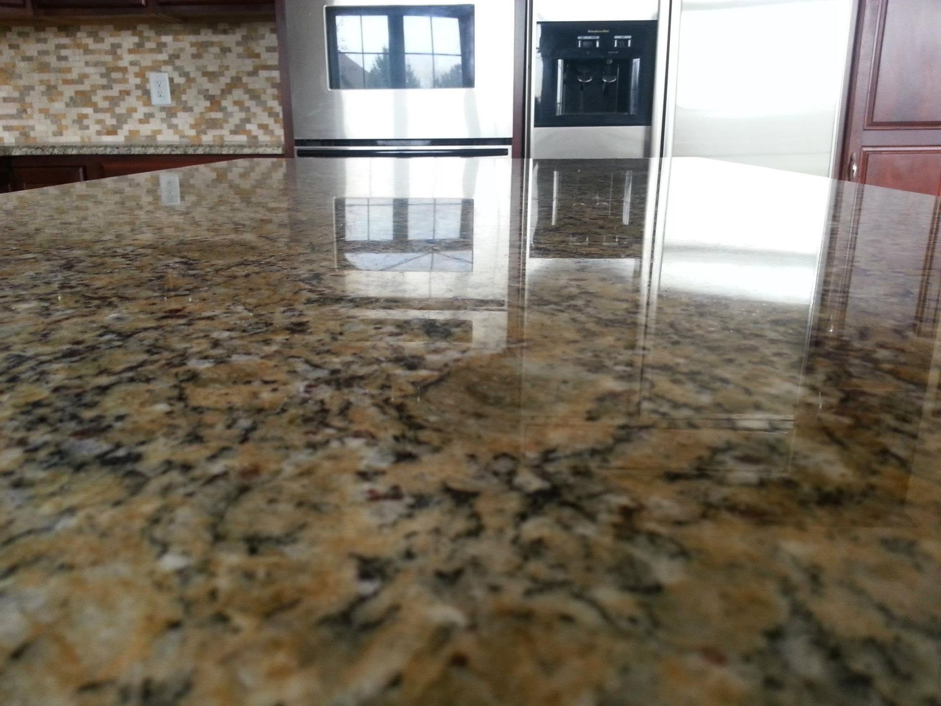 Polished granite countertop reflecting a kitchen or lobby interior with windows and doors