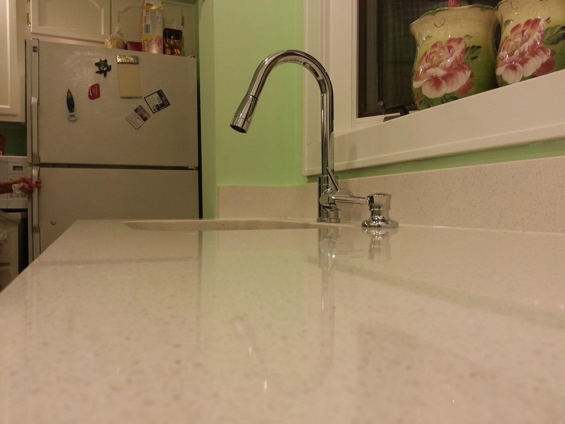 Kitchen counter and sink with chrome faucet, white cabinets, and a refrigerator in the background.