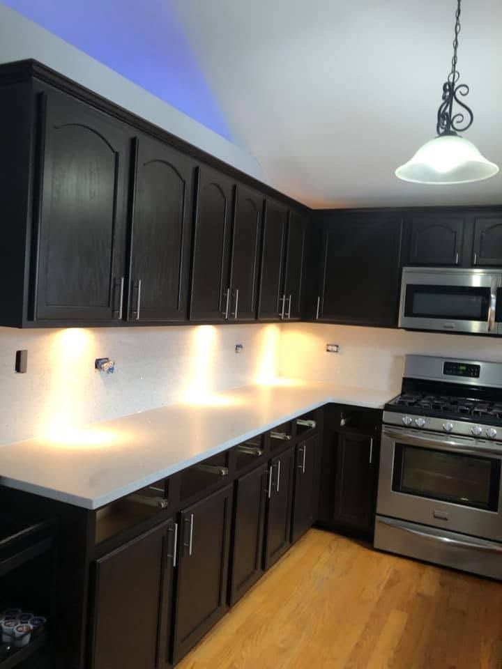 Modern kitchen with dark cabinets, white countertops, stainless steel appliances, and hardwood floors.