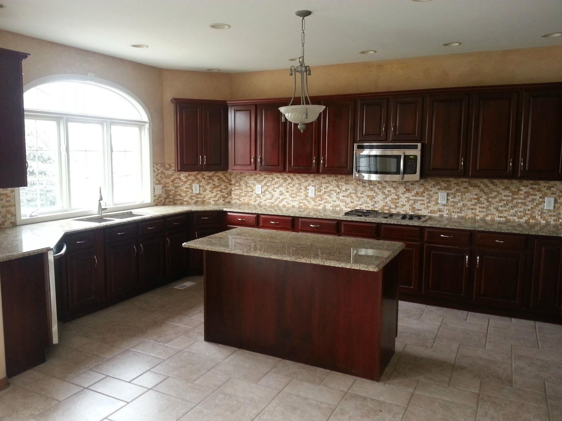 Modern kitchen with dark wood cabinets, large island, tiled floor, and arched window letting in daylight