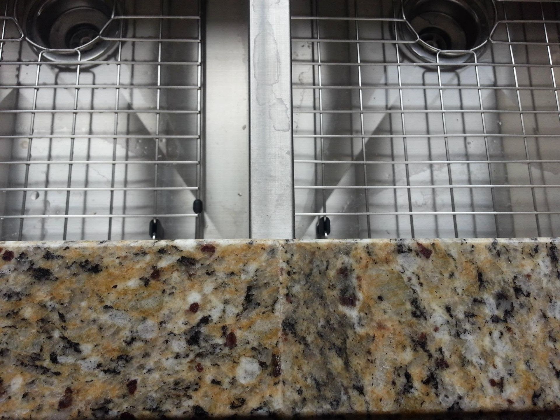 Double kitchen sink with wire drying racks above a speckled granite countertop