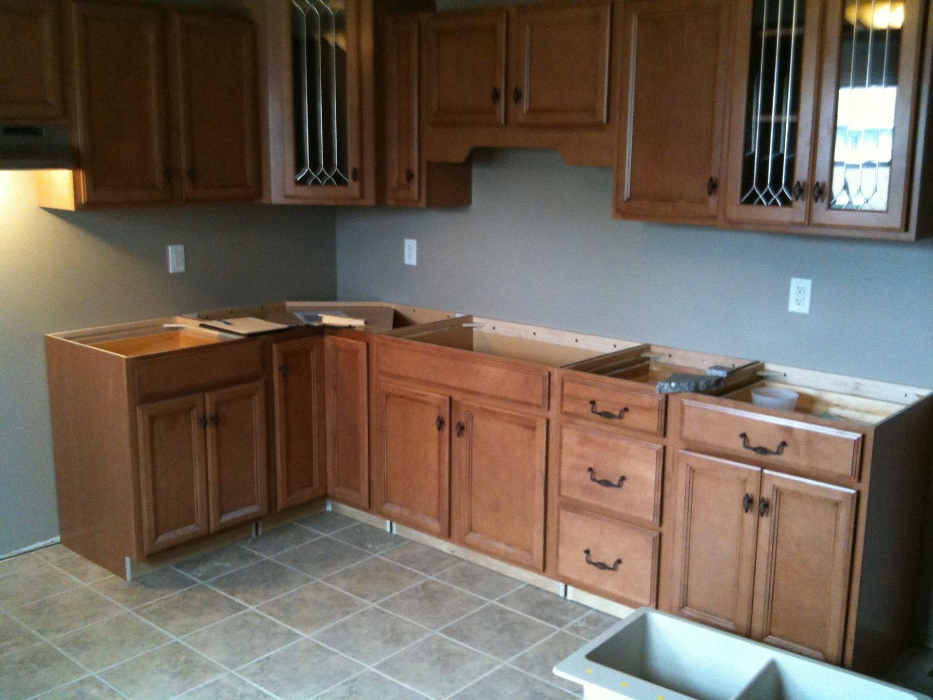 Partially renovated kitchen with wood cabinets, gray walls, tile floor, and a sink under installation