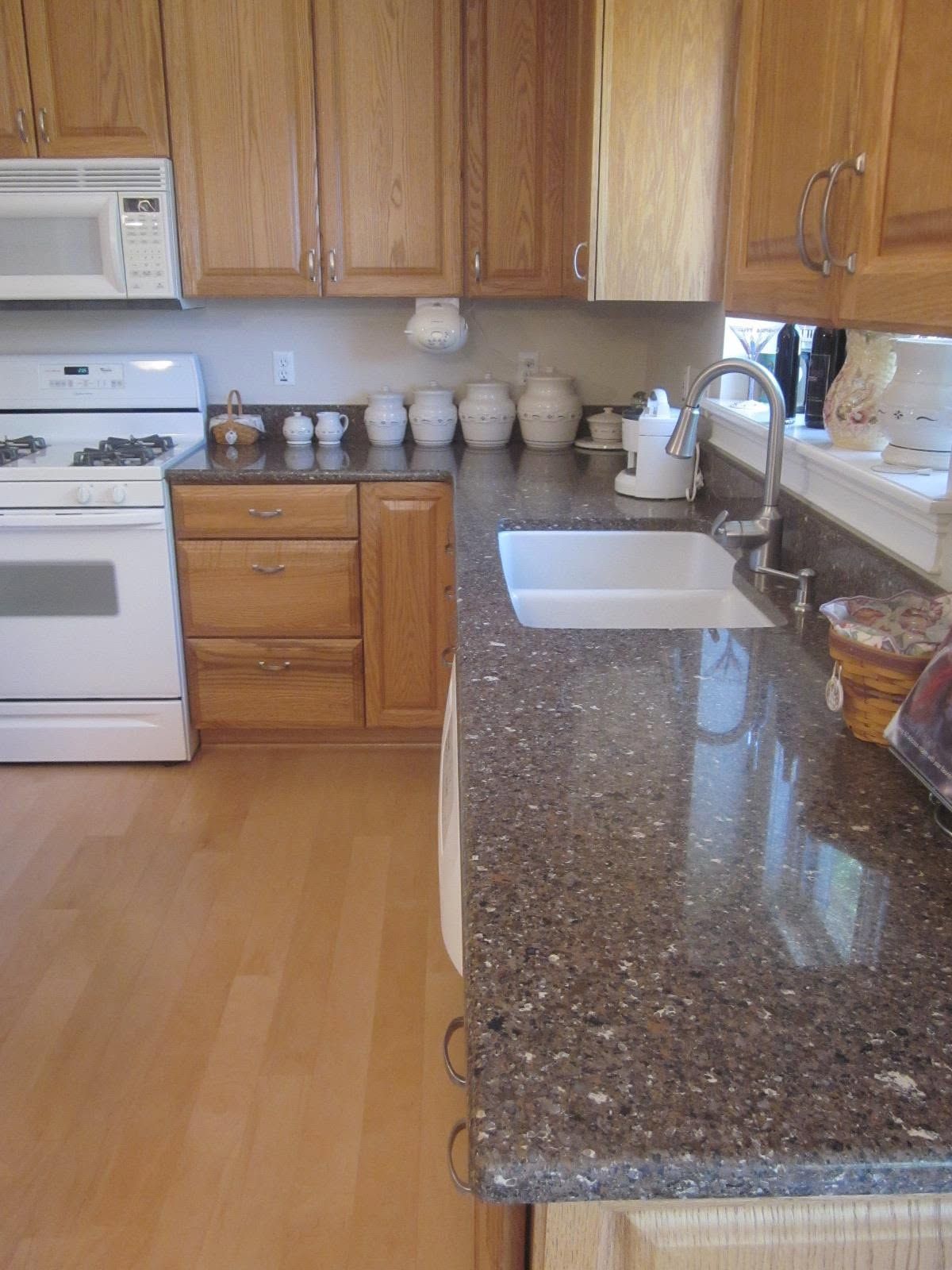 Kitchen with wooden cabinets, white stove, speckled countertop, and sink by a bright window.