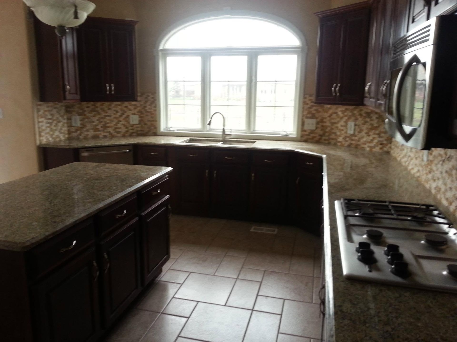 Modern kitchen with dark cabinets, granite counters, tiled backsplash, and a gas stove under a bright window
