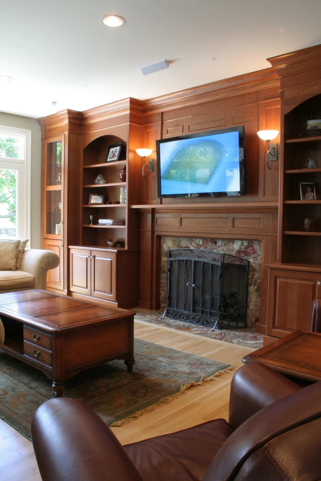 Wood-paneled living room with built-in shelves, fireplace, wall-mounted TV, and leather chairs