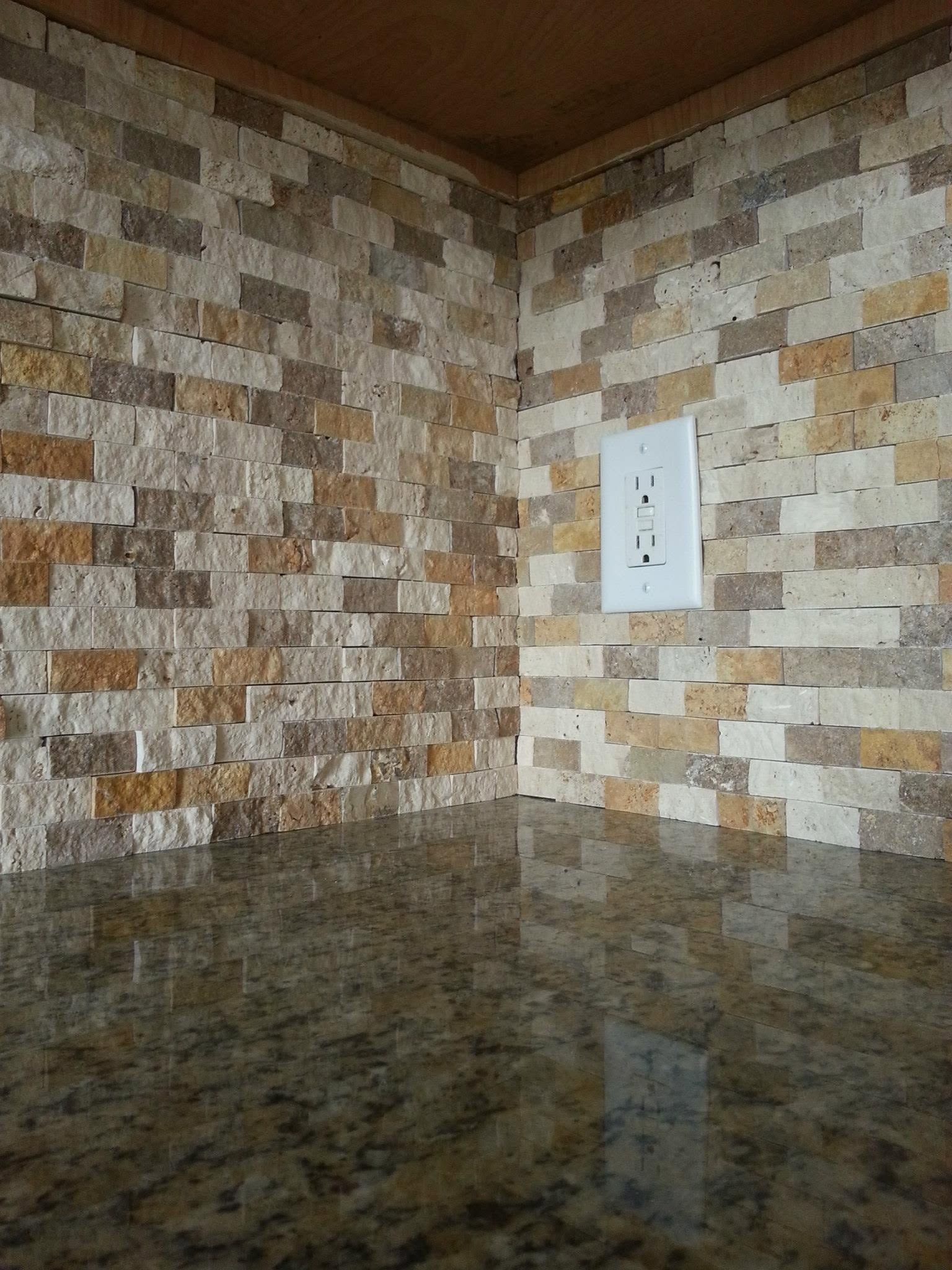 Corner of a kitchen with tiled backsplash and a white electrical outlet above a granite countertop.