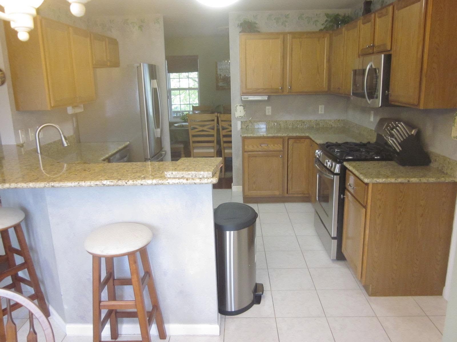 Bright kitchen with wooden cabinets, granite countertops, white tile floor, and stainless steel appliances