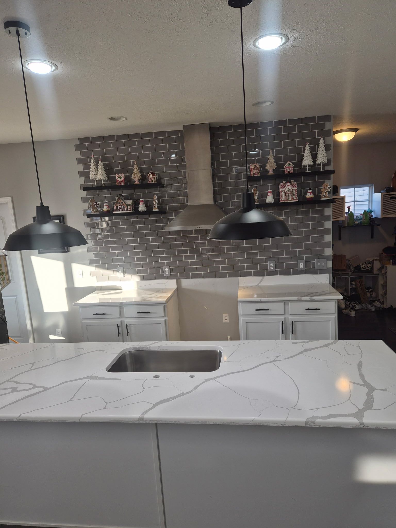 Modern kitchen with white marble island, black pendant lights, and brick backsplash with shelves