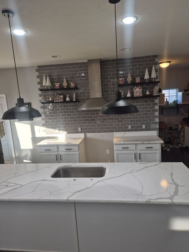 Modern kitchen with white marble island, black pendant lights, and brick backsplash with shelves
