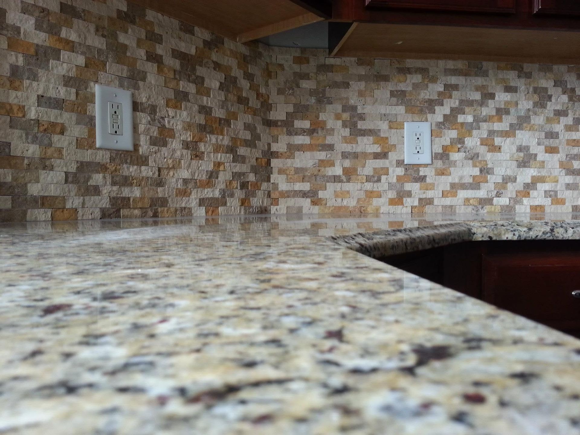 Kitchen countertop with mosaic tile backsplash and wall outlets, viewed from a corner.